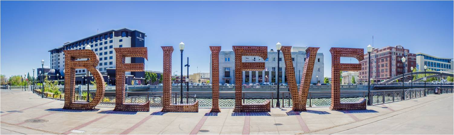 Panoramic image of plaza with large sculptural letters that spell out BELIEVE against the backdrop of buildings