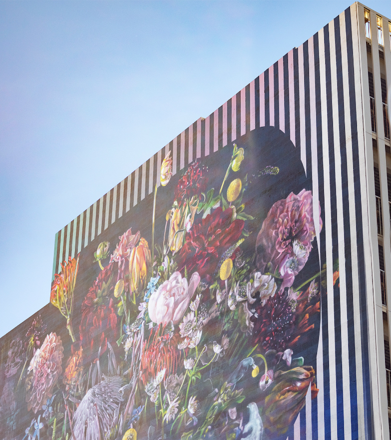 Building against sky with painted mural consisting of a large floral bouquet against a black striped background.