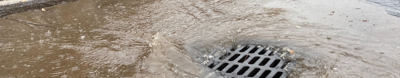 Flooded roadway with water going into storm drain